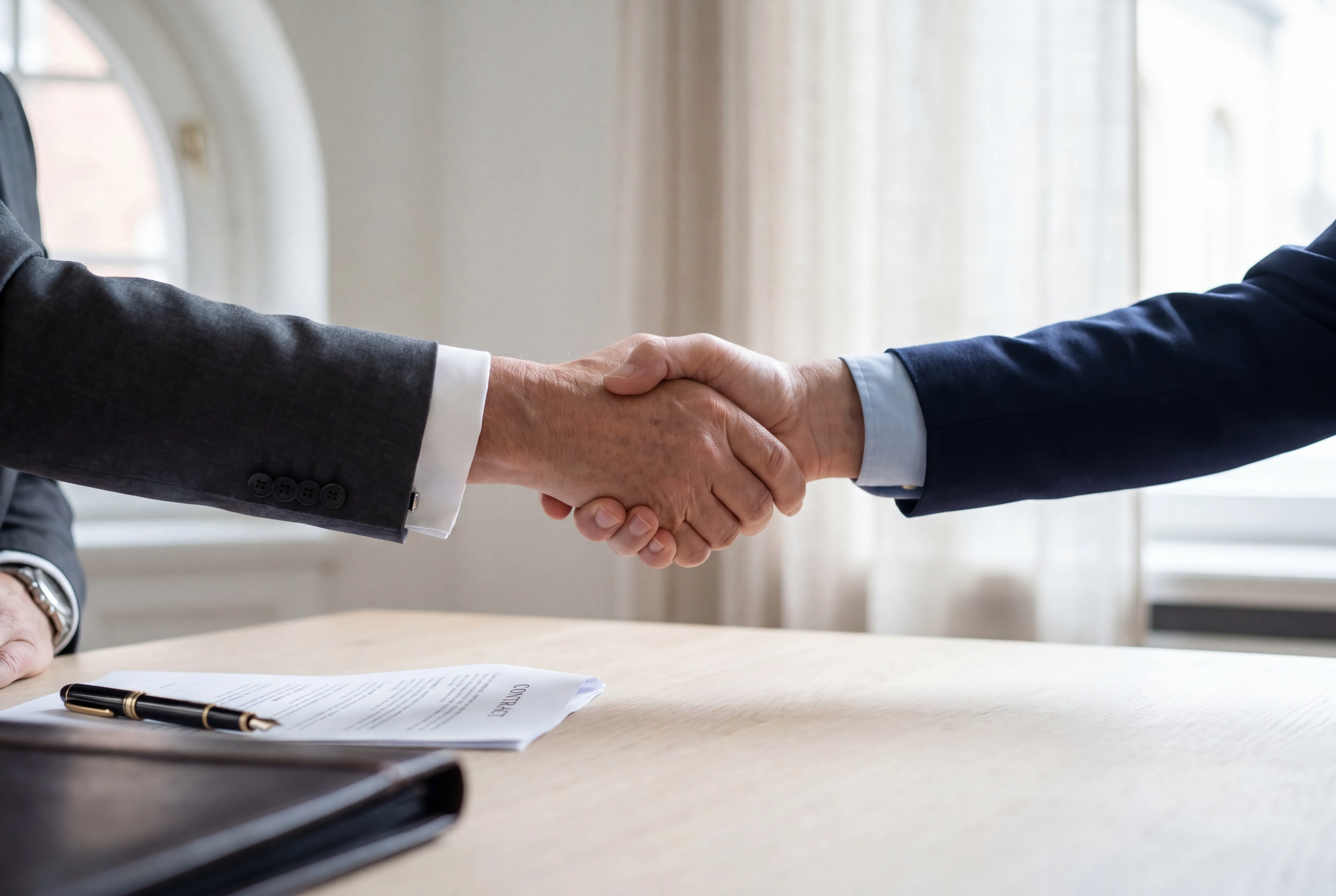 Handschlag zwischen zwei Geschäftspartnern im hellen Boardroom — Symbol für faire Einigung